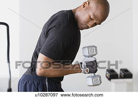 Stock Photo - Young man lifting weights in gym. Fotosearch