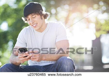 Stock Photography - Young man sitting outdoors, text messaging. Fotosearch