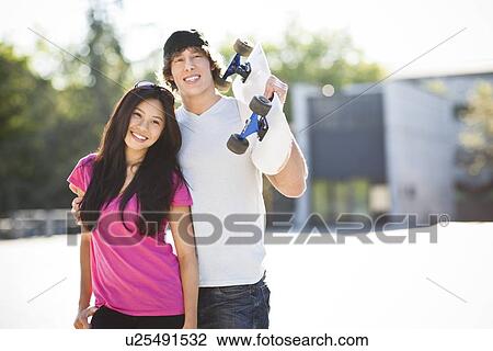 Stock Image - Young multi-racial couple posing with skateboard. Fotosearch
