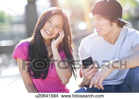 Young multi-racial couple sitting together playing with their mobile phones View Large Photo Image Picture - Young multi-racial couple sitting together playing with their mobile phones. Fotosearch