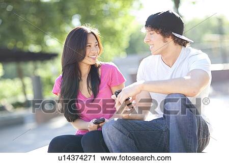 Stock Image - Young multi-racial couple sitting together playing with their mobile phones. Fotosearch
