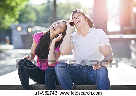 Young multi-racial couple sitting together playing with their mobile phones View Large Photo Image Stock Image - Young multi-racial couple sitting together playing with their mobile phones. Fotosearch
