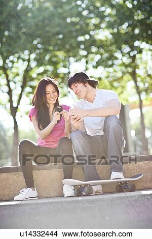 Young multi-racial couple sitting with skateboard, using mobile phone View Large Photo Image Picture - Young multi-racial couple sitting with skateboard, using mobile phone. Fotosearch