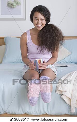 Stock Photo - Young woman sitting on bed. Fotosearch