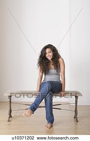 Stock Image - Young woman sitting on bench. Fotosearch