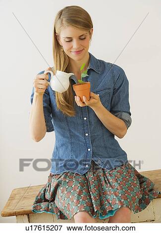 Stock Photo - Young woman watering small plant. Fotosearch
