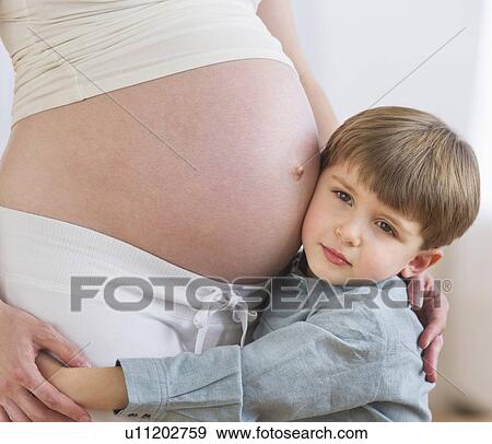 Stock Photo - Boy (4-5) putting ear to pregnant mother's belly. Fotosearch