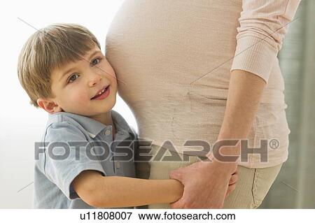 Stock Photo - Boy (4-5) putting ear to pregnant mother's belly. Fotosearch