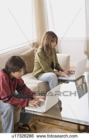 Stock Photograph - Brother and sister using laptops in living room. Fotosearch