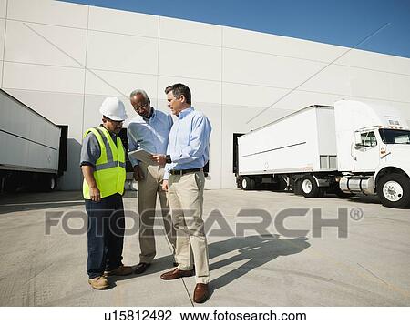 Stock Image - Business men and worker talking outside warehouse. Fotosearch