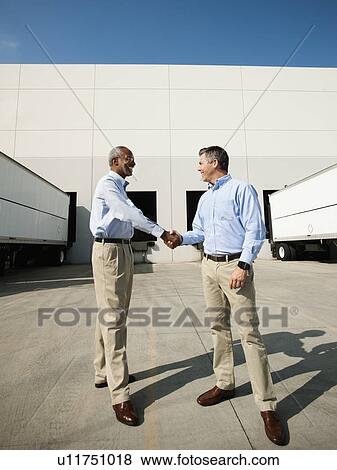 Business men shaking hands outside warehouse View Large Photo Image Stock Photo - Business men shaking hands outside warehouse. Fotosearch