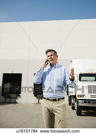 Picture - Businessman talking on phone outside warehouse. Fotosearch