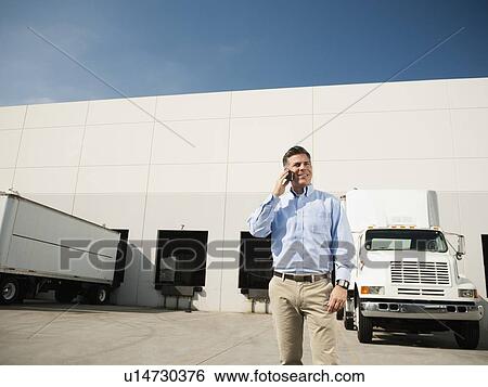 Businessman talking on phone outside warehouse View Large Photo Image Stock Photograph - Businessman talking on phone outside warehouse. Fotosearch
