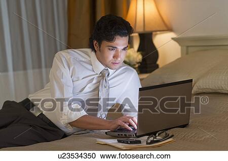 Stock Image - Businessman working on laptop in hotel room. Fotosearch
