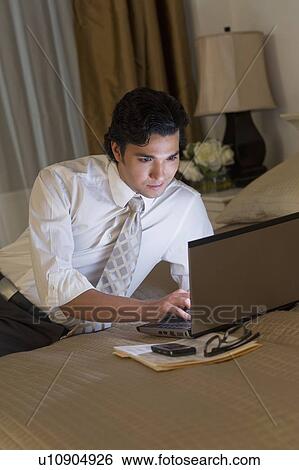 Stock Photograph - Businessman working on laptop in hotel room. Fotosearch