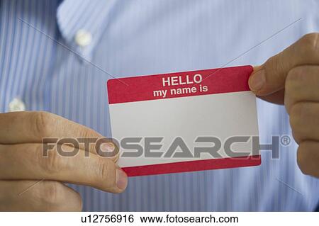Stock Photograph - Close up of businessman's hands holding blank name tag, studio shot. Fotosearch