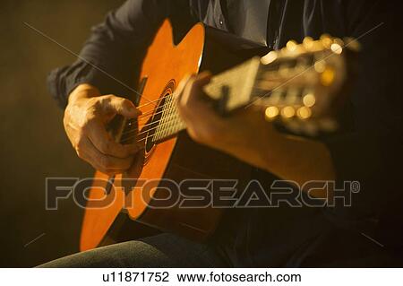 Stock Image - Close up of man playing acoustic guitar, studio shot. Fotosearch