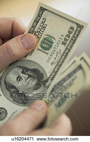 Stock Image - Close up of man's hands counting dollar banknotes. Fotosearch