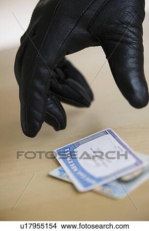 Picture - Close up of thief's hand in black glove stealing driver's license, studio shot. Fotosearch