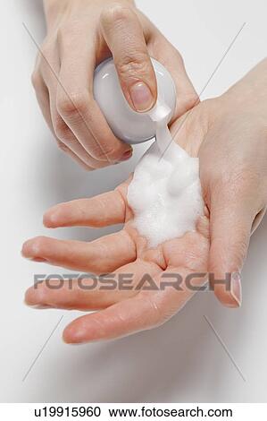 Stock Image - Close up of woman's hands applying moisturizer, studio shot. Fotosearch