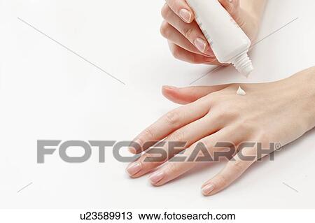 Stock Image - Close up of woman's hands applying moisturizer, studio shot. Fotosearch