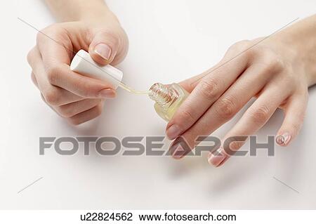 Stock Image - Close up of woman's hands holding nail polish, studio shot. Fotosearch