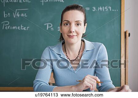 Stock Image - Confident female teacher posing against blackboard. Fotosearch