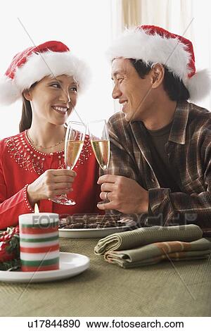 Couple wearing santa hats toasting with champagne View Large Photo Image Stock Image - Couple wearing santa hats toasting with champagne. Fotosearch