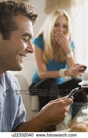 Stock Image - Couples on sofa at home party playing cards. Fotosearch