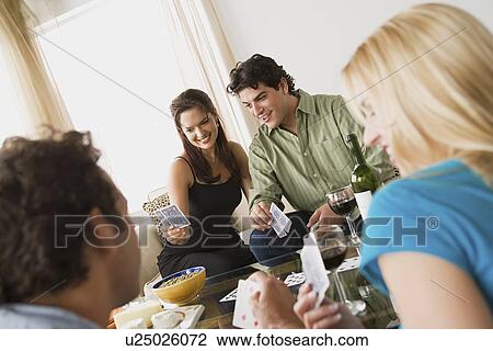 Stock Image - Couples on sofa at home party playing cards. Fotosearch