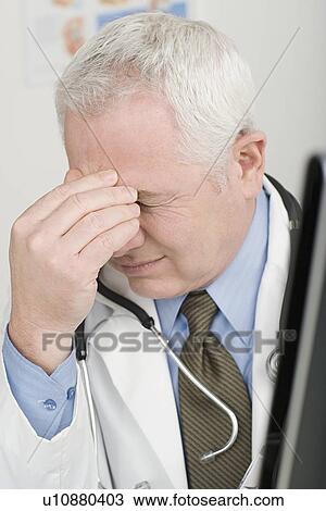 Stock Image - Doctor rubbing forehead. Fotosearch