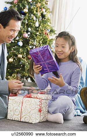 Stock Image - Father and daughter unwrapping christmas gifts. Fotosearch