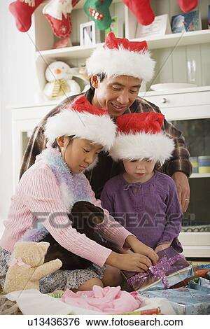 Stock Photograph - Father and daughters (10-11) unwrapping christmas gifts. Fotosearch