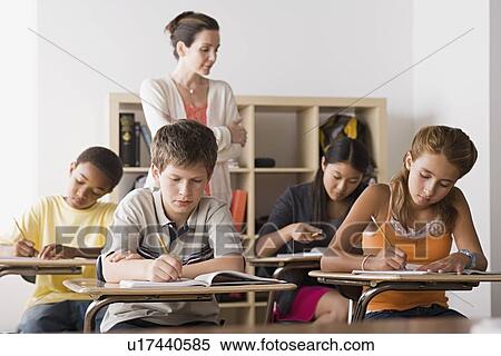 Stock Photography - Female teacher is supervising as class is writing in their copybooks. Fotosearch