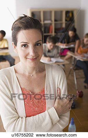 Stock Image - Female teacher posing with class in background. Fotosearch
