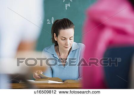 Stock Image - Female teacher standing against blackboard. Fotosearch