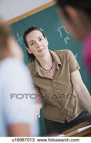 Female teacher standing against blackboard View Large Photo Image Stock Image - Female teacher standing against blackboard. Fotosearch