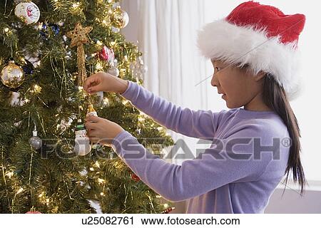 Stock Image - Girl (10-11) decorating Christmas tree. Fotosearch
