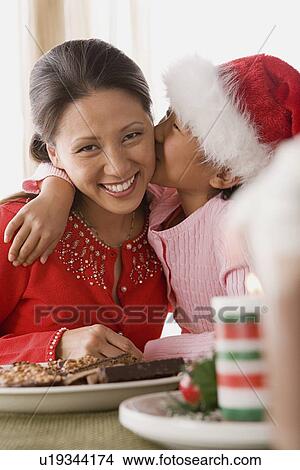 Girl (10-11) wearing Santa hat kissing mother View Large Photo Image Picture - Girl (10-11) wearing Santa hat kissing mother. Fotosearch