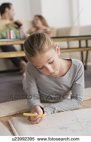 Stock Photography - Girl (12-13) drawing in living room, parents in background. Fotosearch
