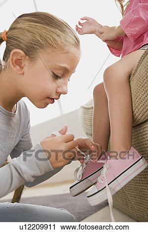 Girl (12-13) tying her younger sister's (8-9) shoes View Large Photo Image Stock Image - Girl (12-13) tying her younger sister's (8-9) shoes. Fotosearch