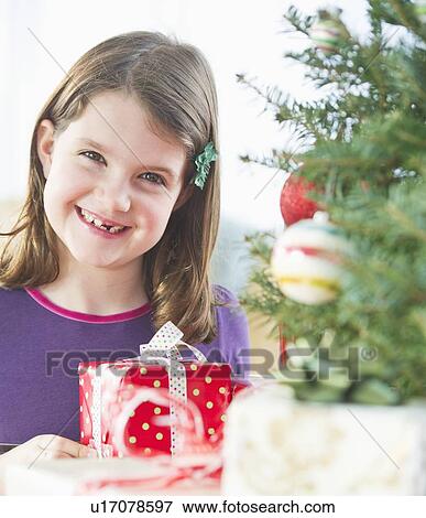 Girl (8-9) standing with gift behind Christmas tree View Large Photo Image Stock Photo - Girl (8-9) standing with gift behind Christmas tree. Fotosearch