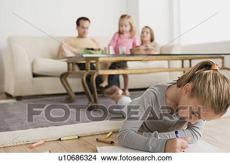 Picture - Girl drawing with family in background. Fotosearch