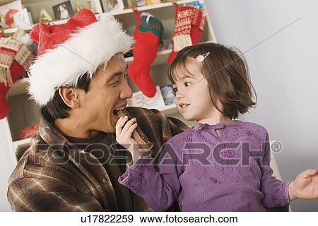 Girl feeding father wearing santa hat View Large Photo Image Stock Photo - Girl feeding father wearing santa hat. Fotosearch