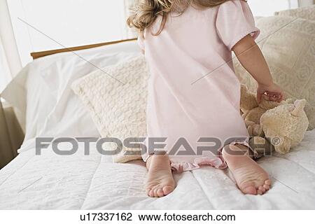 Stock Image - Girl playing with teddy bear in bed. Fotosearch