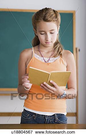 Girl reading from book in front of blackboard View Large Photo Image Stock Photo - Girl reading from book in front of blackboard. Fotosearch