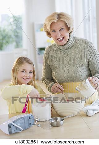 Stock Image - Grandmother with granddaughter (8-9) preparing food. Fotosearch