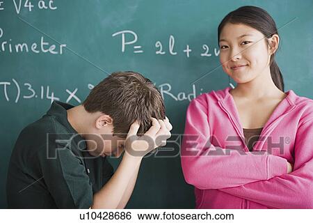 Stock Photograph - Happy girl and frustrated boy standing in front of blackboard with mathematical formula. Fotosearch