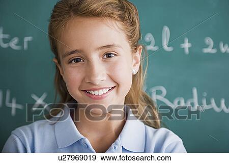Stock Photo - Happy schoolgirl posing in front of blackboard. Fotosearch