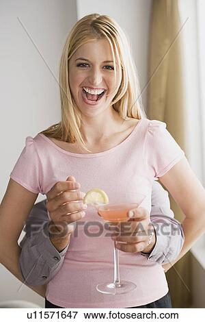 Stock Photo - Man behind laughing woman holding cocktail. Fotosearch